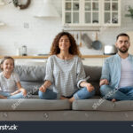stock-photo-calm-young-family-with-little-daughter-sit-on-couch-practice-yoga-together-happy-parents-with-1660546054