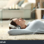 stock-photo-side-view-portrait-of-a-relaxed-woman-listening-to-music-with-headphones-lying-on-a-carpet-at-home-1886423599